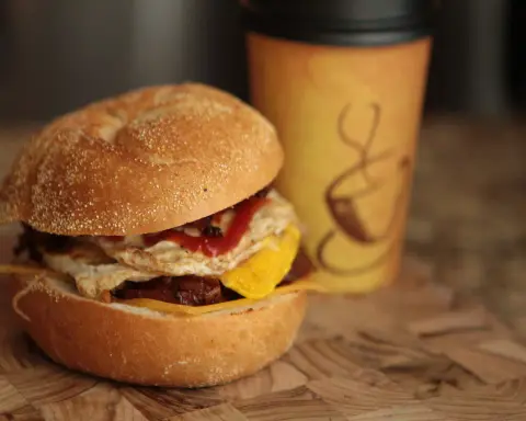 Breakfast sandwich with bacon, egg and cheese alongside fresh coffee