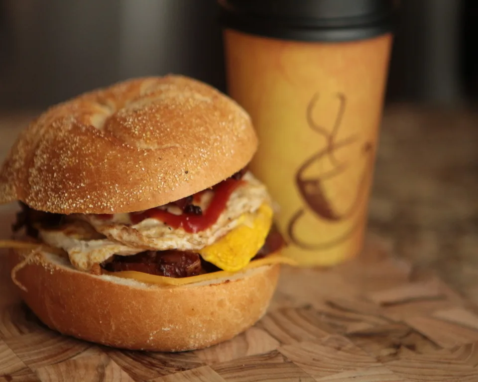 Breakfast sandwich with bacon, egg and cheese alongside fresh coffee